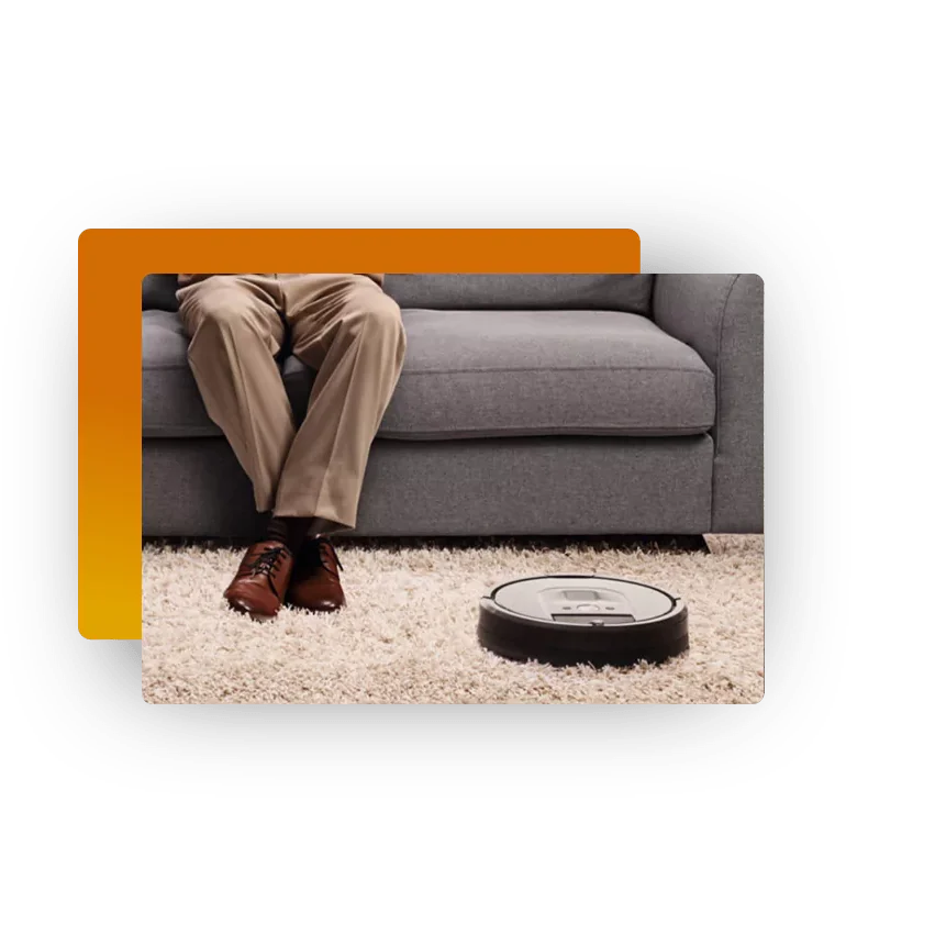 Man sitting on a sofa while a robot vacuum cleans the carpet in front of him