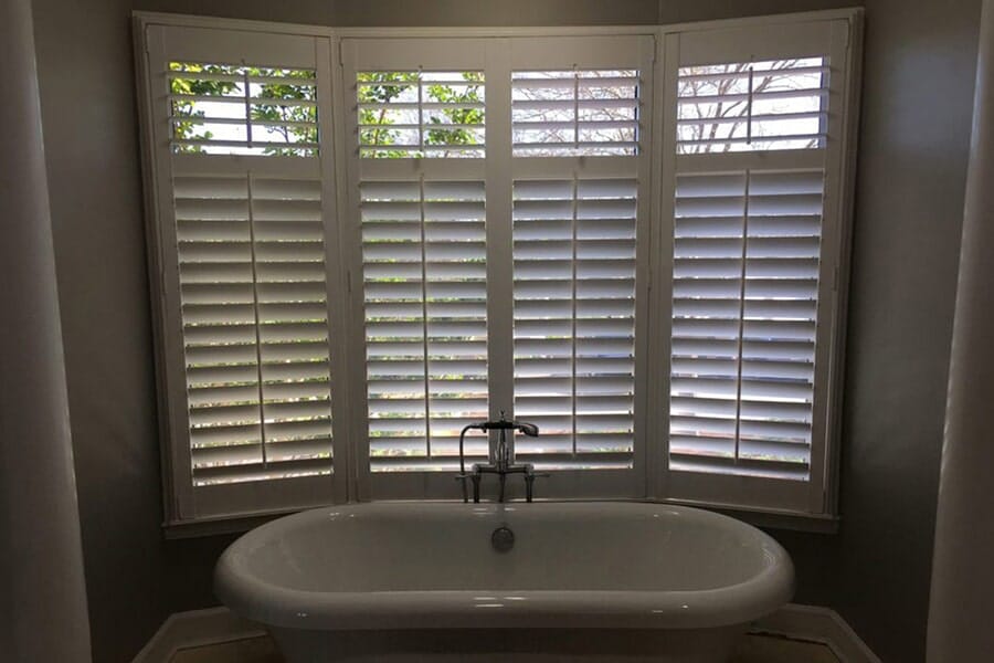 Bathroom with large window featuring plantation shutters