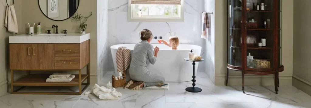 Mother giving a bath to her daughter sitting on tile flooring