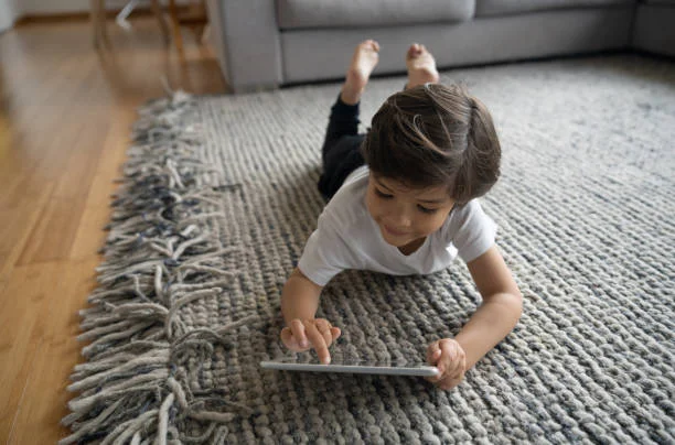 Girl laying on grey area rug playing on her ipad